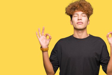 Siyah t-shirt dinlenmek giydiği ve gülümseyen gözlerle afro saçlı yakışıklı delikanlı parmak ile meditasyon jest yapıyor kapalı. Yoga kavramı.