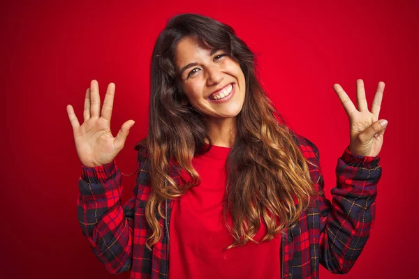 赤い孤立した背景の上に立つカジュアルなジャケットを着た若い美しい女性は サインを通して微笑む手と指でハートの形をしています — ストック写真