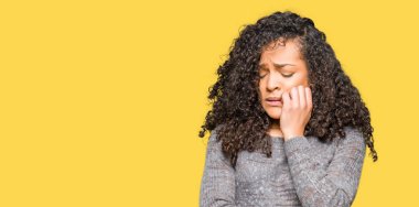 Kıvırcık saçlı genç güzel kadın gri kazak görünümlü stresli ve ağız tırnak ısırma elleri ile sinir. Anksiyete sorunu.