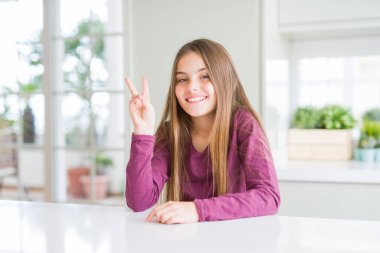 Beyaz masa üzerinde güzel genç kız çocuk gösteren ve parmakları ile işaret ederken iki numara kendinden emin ve mutlu gülümseyerek.