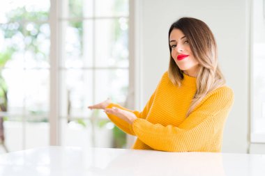 Evde kış kazak giyen genç güzel kadın açık el ile doğal gülümseyen girmek için davet