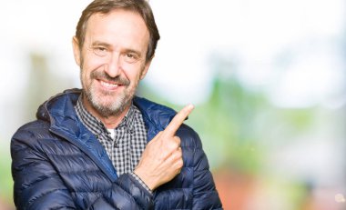 Orta yaş yakışıklı adam neşeli bir gülümseme ile el ve parmak kadar yan yüzünde mutlu ve doğal ifade ile işaret yüz ile bir kış palto giyiyor