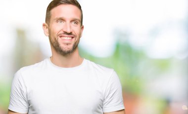 Yakışıklı adam uzak tarafına yüzünde, doğal ifade gülümseme ile seyir casual beyaz t-shirt giyiyor. Kendine güvenen gülüyor.