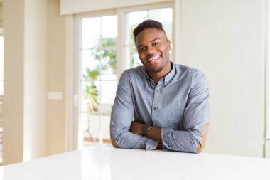 Afro-Amerikan yakışıklı beyaz masa mutlu yüz çapraz silah kameraya bakarak ile gülümseyen. Olumlu bir kişi.