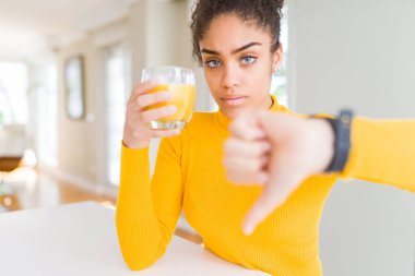 Genç afro-amerikan kadın kızgın yüz ile taze portakal suyu bir bardak içme, başparmak aşağı, ret kavramı ile sevmediğimi gösteren negatif işareti