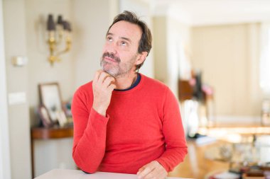Yakışıklı orta yaş erkek evde ile el çeneme soru dalgın ifade hakkında düşünme. Düşünceli yüzüyle gülümsüyor. Şüphe kavramı.
