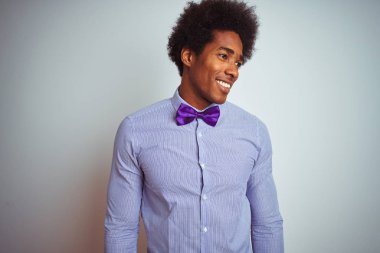 Afro iş adamı çizgili gömlek ve izole beyaz arka plan üzerinde mor papyon giyen yüzünde gülümseme, doğal ifade ile yan bakıyor. Gülmekten emin.