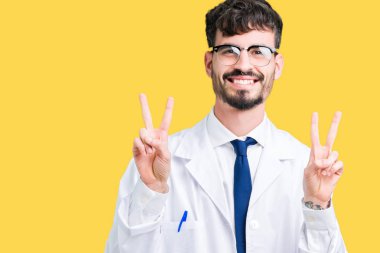 Zafer işareti yapıyor parmak gösterilen kamera seyir gülümseyen izole arka plan üzerinde beyaz önlük giyen genç profesyonel bilim adam. İki numaralı.