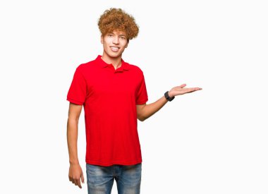 Neşeli sunulması ve kameraya bakarak avucunun ile işaret gülümseyen kırmızı t-shirt giyen afro saçlı Genç yakışıklı adam.