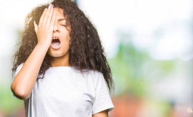 Rahat beyaz t-shirt giyen kıvırcık saçlı Genç güzel kız yarı yüz, göz ve el ile ağız kapsayan yorgun esneme. Yüz acı acıyor.