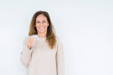 Orta yaş kadın bardak su içme arka plan ayakta ve diş gösterilen kendine güvenen bir gülümsemeyle gülümseyerek mutlu bir yüz ile izole