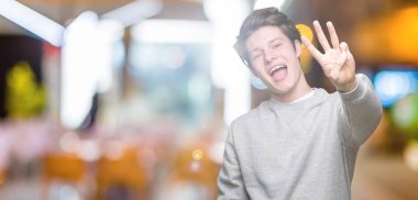 Gösterilen arka plan üzerinde sweatshirt giyen genç yakışıklı sportif adam izole ve parmakları ile işaret kendinden emin ve mutlu gülümseyerek iken üçüncü.