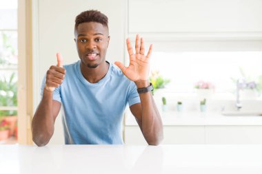 Yakışıklı afro-amerikan adam evde gösteren rahat t-shirt giyen ve parmakları ile işaret ederken kendinden emin ve mutlu gülümsüyor.