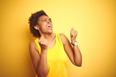 Beauitul afro-amerikan kadın izole sarı arka plan üzerinde yaz t-shirt giyen çok mutlu ve heyecanlı kolları kaldırdı ile kazanan jest yapıyor, gülümseyerek ve başarı için çığlık. Kutlama konsepti.