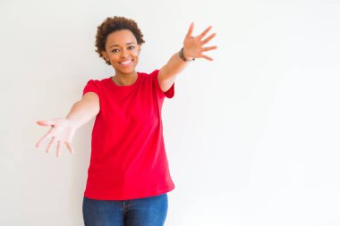 Beyaz arka plan üzerinde genç güzel afro-amerikan kadın sarılmak için açık kollarla gülümseyen kameraya bakıyor. Mutluluğu kucaklayan neşeli ifade.