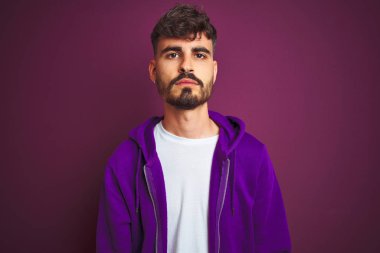 Yüze ciddi ifade ile izole sarı arka plan üzerinde ayakta çizgili polo giyen dövme ile genç adam. Basit ve doğal kamera bakıyor.