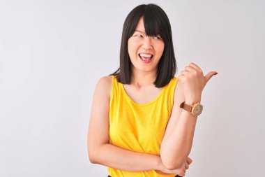 Genç güzel Çinli kadın izole beyaz arka plan üzerinde sarı t-shirt giyen mutlu yüz görünümlü gülümseyerek ve başparmak ile yan işaret.