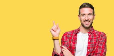 Yakışıklı adam, yüzünde kocaman bir gülümseme ile rahat gömlek giymiş kameraya bakarak yan el ve parmak ile işaret.