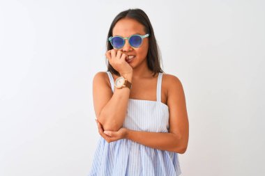İzole beyaz arka plan üzerinde çizgili elbise ve güneş gözlüğü giyen genç Çinli kadın stresli ve ağız tırnak ısırma elleri ile sinirli görünümlü. Anksiyete sorunu.