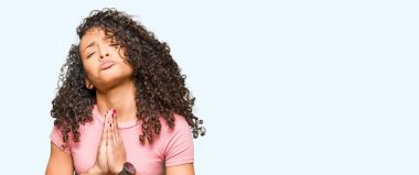 Kıvırcık saçlı Genç güzel kadın pembe t-shirt yalvarıyor ve elleri ile birlikte dua yüz çok duygusal ve endişeli üzerinde umut ifade giyiyor. Affedilmesini istiyorum. Din konsepti.