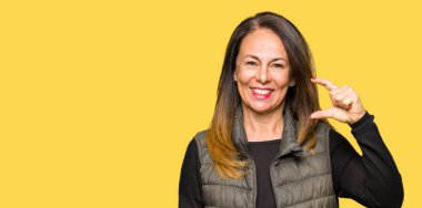 Güzel orta yaş giyen kış yelek gülümseyen kadın ve kendine güvenen boyutu işi el ile eller parmakları ile süre seyir ve kamera oturum açın. Ölçü kavramı.