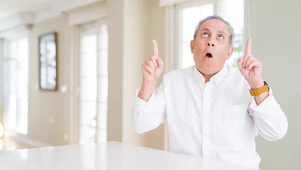 Hombre Mayor Guapo Casa Asombrado Sorprendido Mirando Hacia Arriba Señalando —  Fotos de Stock