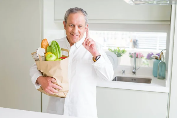 부엌에서 신선한 식료품의 가방을 노인은 행복한 손가락을 가리키는 아이디어 질문으로 — 스톡 사진