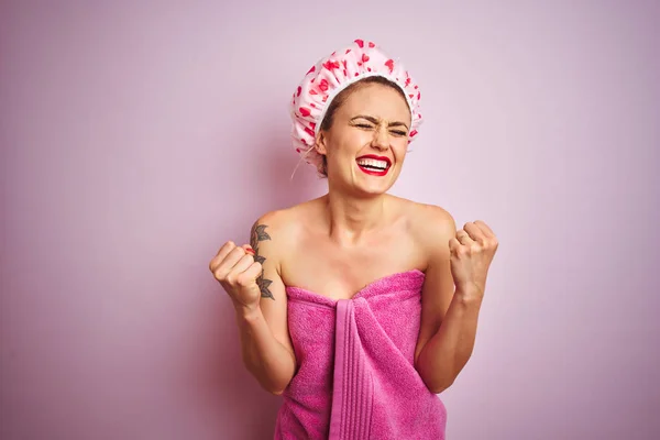 年轻的漂亮女人穿着毛巾和浴帽后淋浴在粉红色孤立的背景兴奋的成功与手臂抬起和眼睛闭上庆祝胜利微笑 优胜者概念 — 图库照片