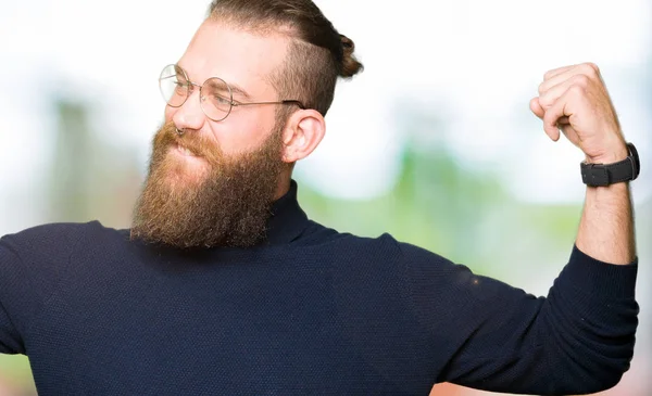 Gözlük ve kol kasları gururlu gülümseyen gösterilen boğazlı kazak giyen genç sarışın adam. Fitness kavramı.