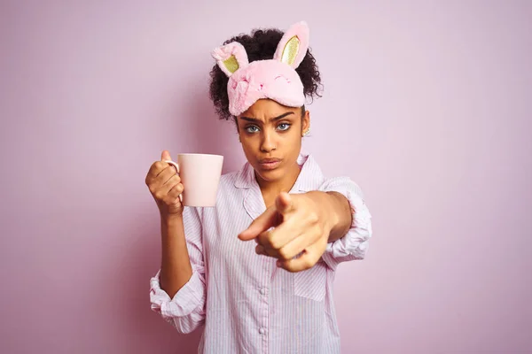 非洲妇女穿着睡衣和面具喝一杯咖啡 在孤立的粉红色背景用手指指着相机和你 手标志 积极和自信的姿态从前面 — 图库照片