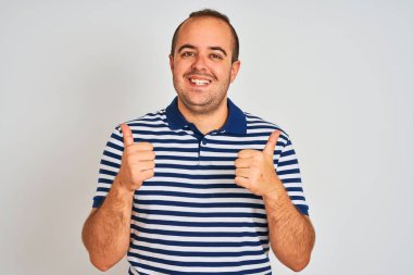 Izole beyaz arka plan başarı işareti el ile olumlu jest yapıyor üzerinde duran rahat çizgili polo giyen genç adam, gülümseyerek ve mutlu başparmak kadar. Neşeli ifade ve kazanan jest.