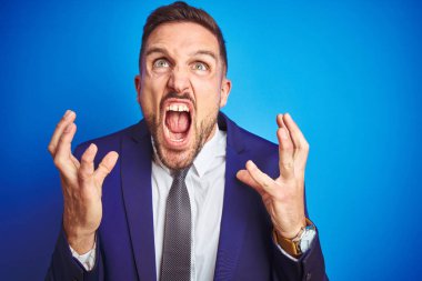 Mavi izole arka plan deli ve deli bağırarak ve agresif ifade ve kollar kaldırdı ile bağırıyor üzerinde genç yakışıklı iş adamı yakın resmi. Hayal kırıklığı kavramı.