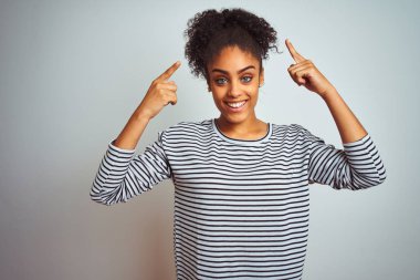 Izole beyaz arka plan üzerinde duran lacivert çizgili t-shirt giyen Afrikalı Amerikalı kadın iki eliyle parmak, harika bir fikir ya da düşünce, iyi bellek ile baş gösteren gülümseyerek