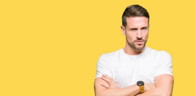 Yakışıklı adam rahat beyaz t-shirt şüpheci ve sinir, kesişmiş kollar ile yüz üzerindeki ifade onaylanmaz giyiyor. Negatif kişi.