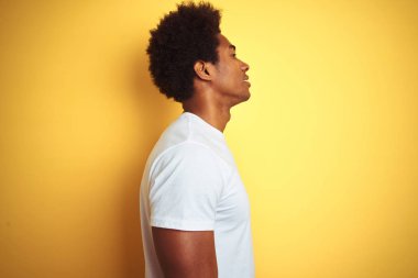 Beyaz saçlı afro saçlı Amerikalı adam yan bakarak izole sarı arka plan üzerinde duran beyaz t-shirt giyen, kendine güvenen gülümseme ile doğal yüz ile profil poz dinlenmek.