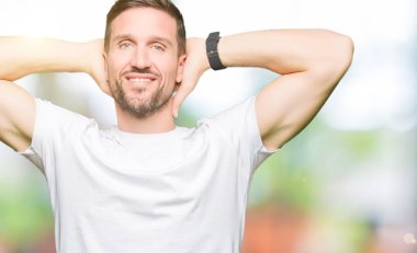 Yakışıklı adam rahat beyaz t-shirt dinlenirken ve germe kollar ve eller baş ve boyun arkasında ile mutlu gülümseyerek