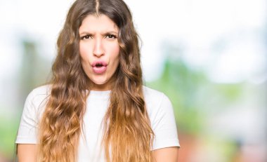 Genç güzel kadın rahat beyaz t-shirt korkuyor ve sürpriz ifade, korku ve heyecanlı yüz ile şok giyiyor.