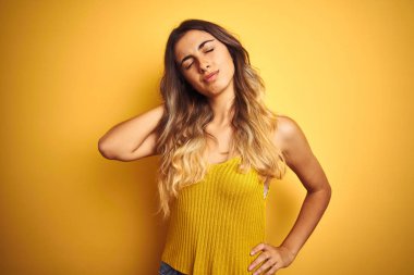 Genç güzel kadın sarı izole arka plan üzerinde t-shirt giyen boyun ağrısı yaralanma acı, el ile boyun dokunmadan, kas ağrısı