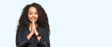 Kıvırcık saçlı Genç güzel kız el ile birlikte AF gülümseyen emin gülümsüyor isteyen dua zarif elbise giyiyor.