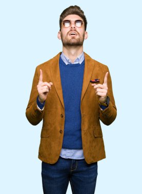 Genç yakışıklı şık erkek güneş gözlüğü takıyor hayrete ve yukarıya bakıyor ve parmakları ile işaret ve silah kaldırdı şaşırttı.