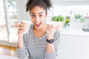 Genç afro-amerikan kız bir götürmek kağıt fincan bir kahve içme işaret ve mutlu yüzü gülümseyerek yan başparmak ile gösteren