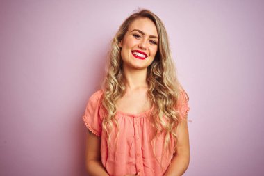 Genç güzel kadın elleri birlikte pembe izole arka plan üzerinde duran t-shirt giyen ve rahat ve neşeli gülümseyen parmakları geçti. Başarı ve iyimser