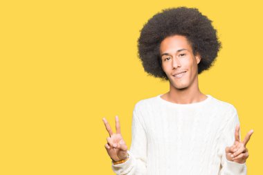 Afrikalı-Amerikalı genç afro saç giyen kış kazak zafer işareti yapıyor parmak gösterilen kamera seyir gülümseyerek. İki numaralı.