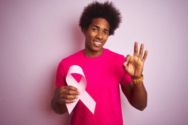Genç afro-amerikan adam izole pembe arka plan üzerinde parmakları, mükemmel sembolü ile ok işareti yapıyor ayakta kanser kurdele tutan