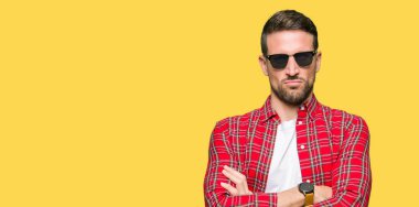 Yüz çapraz kolları olan moda güneş gözlüğü şüpheci ve sinir, onaylamayan ifade giyen yakışıklı adam. Negatif kişi.