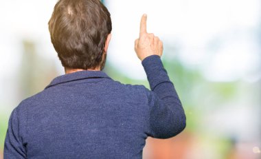 Bir kazak geriye doğru poz giyen orta yaş yakışıklı adam arkasında parmak eliyle işaret