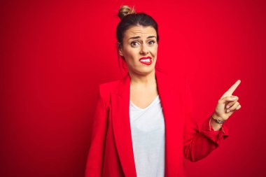 Genç güzel iş kadını kırmızı izole arka plan üzerinde duran işaret parmağı ile endişeli ve sinirli bir kenara işaret, endişeli ve sürpriz ifade