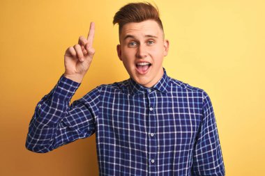 Genç yakışıklı adam başarılı bir fikir ile parmak işaret izole sarı arka plan üzerinde duran rahat gömlek giyiyor. Çıktı ve mutlu. Bir numara.
