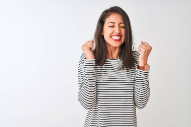 İzole beyaz arka plan üzerinde duran çizgili t-shirt giyen genç güzel Çinli kadın kollarını kaldırdı ve gözleri gülümseyerek zafer kutluyor kapalı başarı için heyecanlı. Kazanan kavramı.