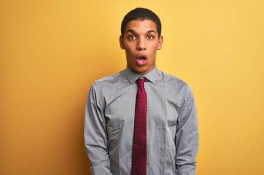 Genç yakışıklı Arap işadamı gömlek giyen ve izole sarı arka plan üzerinde kravat korkmuş ve sürpriz ifade ile şok, korku ve heyecanlı yüz.